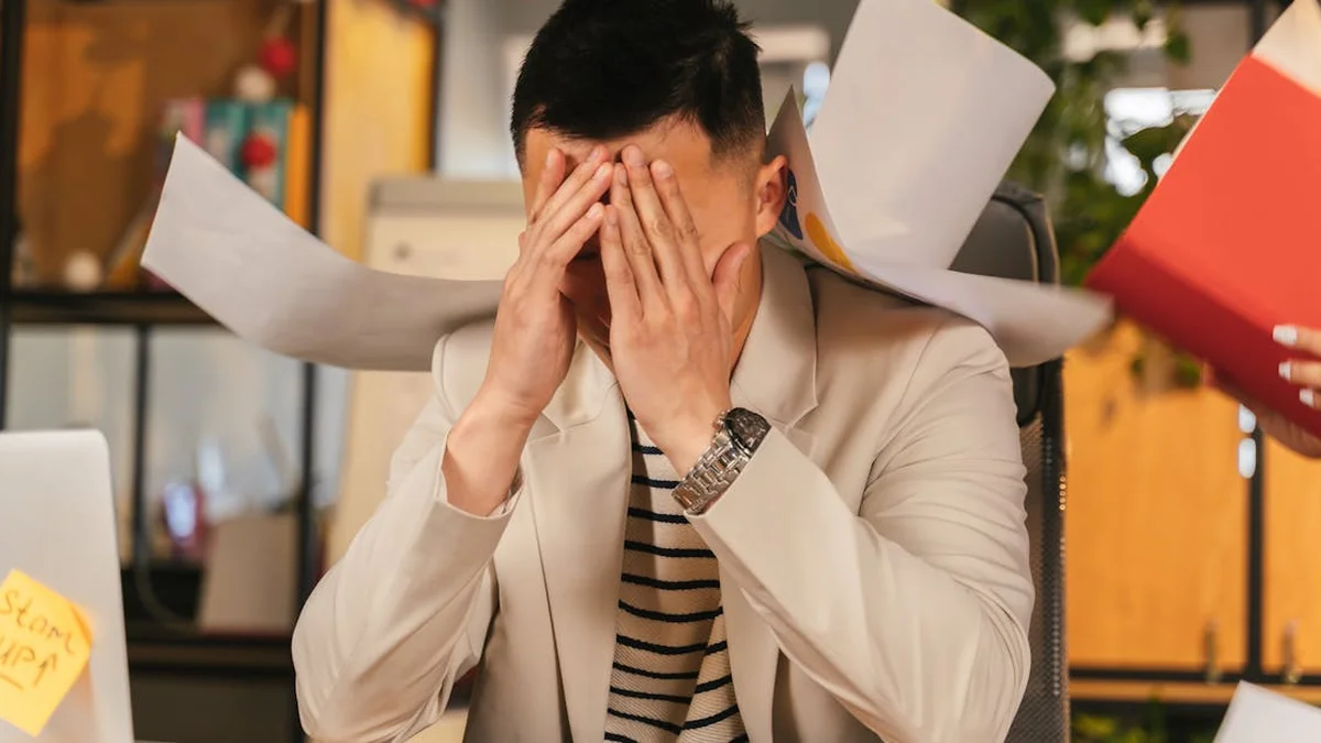 Ansiedad laboral en adultos: cuando el trabajo se siente com - Stressed businessman overwhelmed by paperwork in office environment, demonstrati