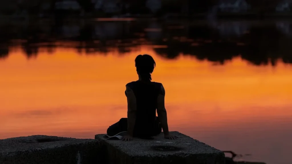 El sistema de bloques de tiempo que transforma tu concentrac - A person meditates at sunrise by a calm lake, creating a serene silhouette.