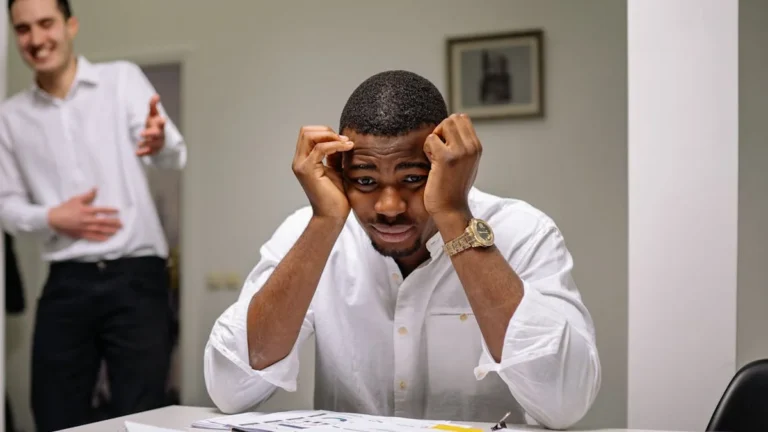 Señales de que estás en modo urgencia permanente y cómo sali - Tensed businessman at desk while coworker is laughing. Office stress concept.