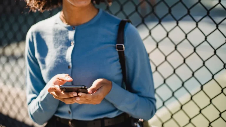 Perfil de Instagram optimizado: la base de tu crecimiento en - A cheerful woman uses her smartphone outdoors near a fence.