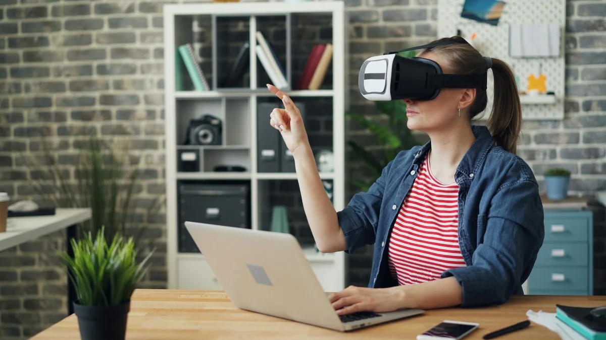 Cómo configurar tareas programadas con IA: tutorial para que... — A woman using a VR headset while working on a laptop, exploring virtual reality