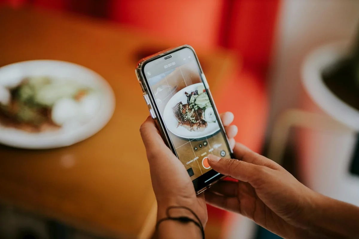 Cómo optimizar tu perfil de TikTok en 2026: tutorial paso a... — Close-up of a person using a smartphone to photograph food in a cozy indoor sett