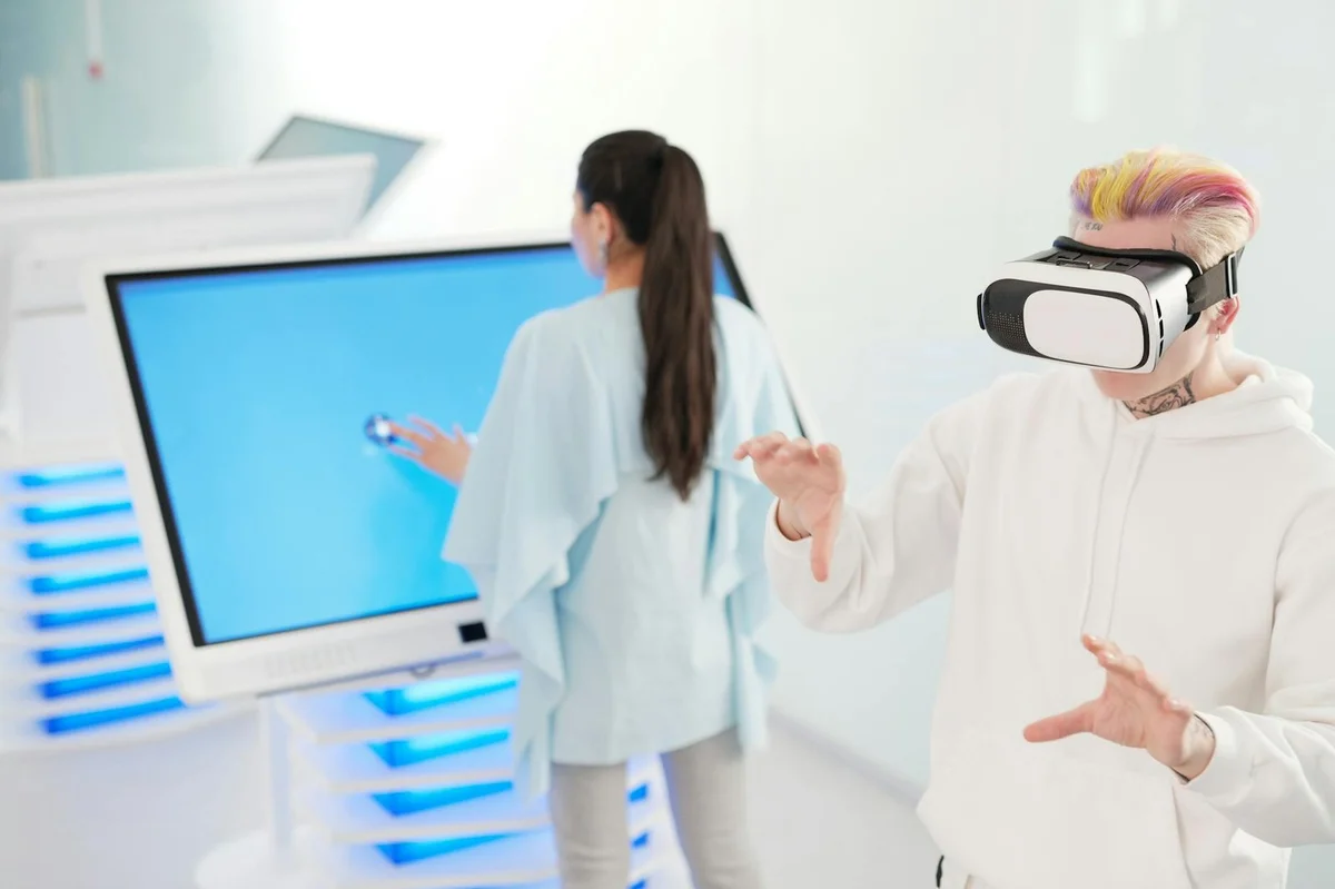 Cómo auditar tus decisiones con IA: tutorial paso a paso par... — Two young adults engaging with VR and touchscreen technology in a futuristic roo