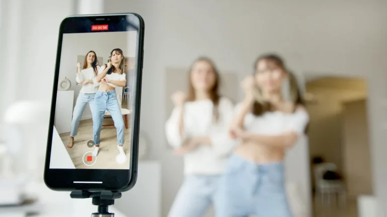 Cómo convertir TikTok en negocio: tutorial de monetización p... — Two women dance in front of a smartphone camera, recording content indoors.