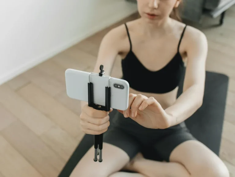 Cómo funciona el algoritmo de TikTok en 2026: tutorial paso... — A woman using a smartphone on a tripod to film her yoga session indoors.