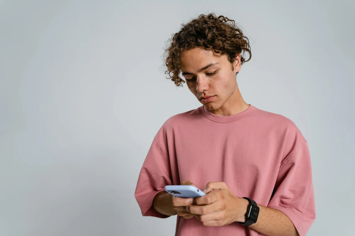 How to Build a Loyal TikTok Community: From Audience to Peop... — Teenager with curly hair using a smartphone indoors, wearing a pink t-shirt.
