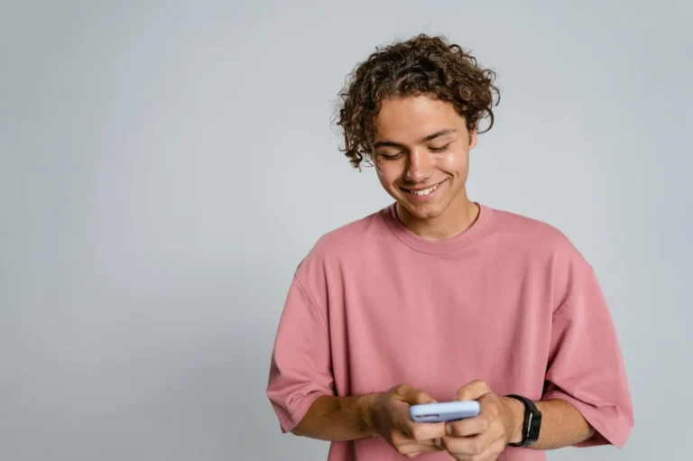 Cómo escribir guiones naturales para TikTok: tutorial paso a... — Teenager with curly hair smiling down at smartphone in a studio setup.