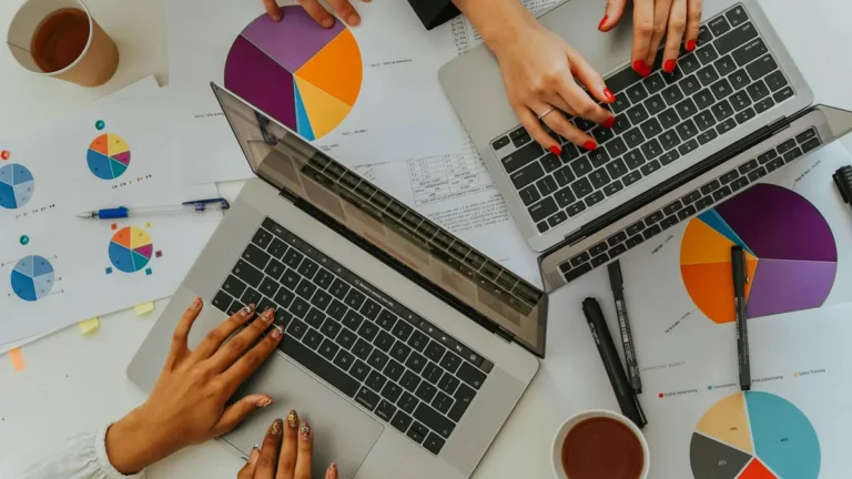 Overhead view of a team analyzing graphs and charts using laptops at a meeting.