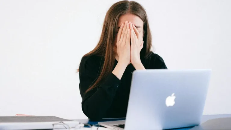 Woman feeling stressed and overwhelmed at her desk while working remotely on a laptop.