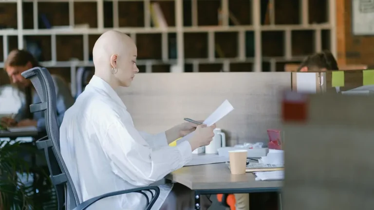 Side view of focused bald female office worker sitting at table and reading document while working i