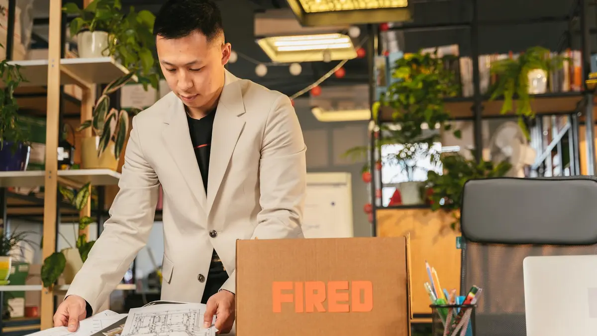 An employee packing documents into a box labeled 'FIRED' in an office environment.