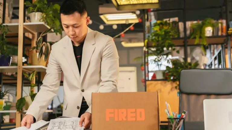 An employee packing documents into a box labeled 'FIRED' in an office environment.