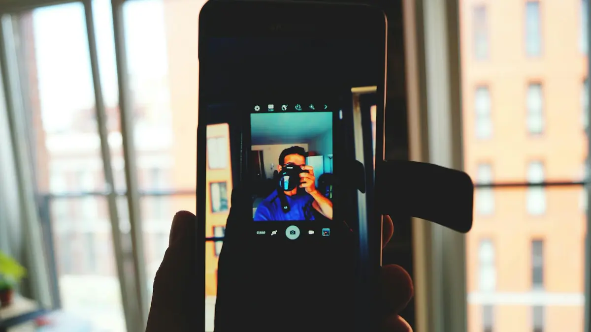 A man takes a smartphone selfie capturing his own reflection in an indoor urban setting.