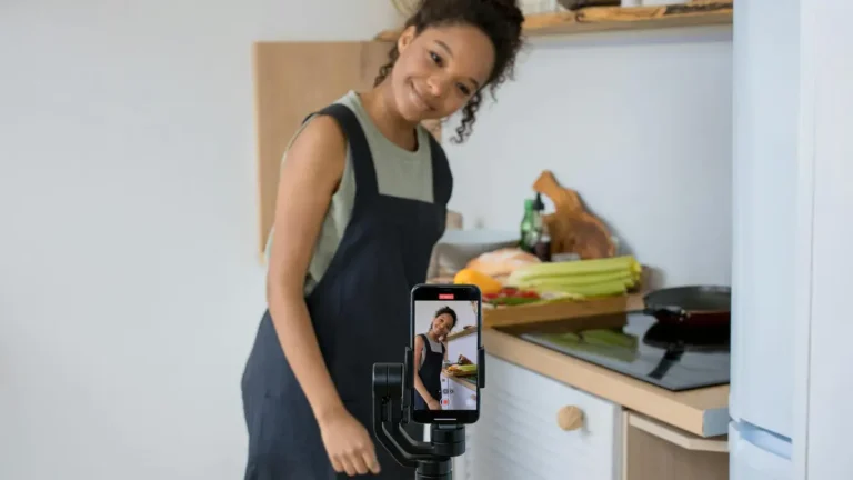 Smiling young woman films a cooking video at home using a smartphone in her kitchen.