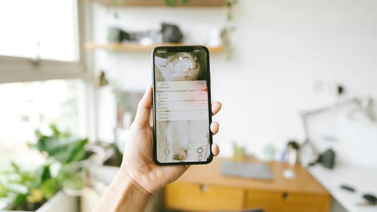 Hand holding smartphone indoors with blurred office background, focus on screen notifications.