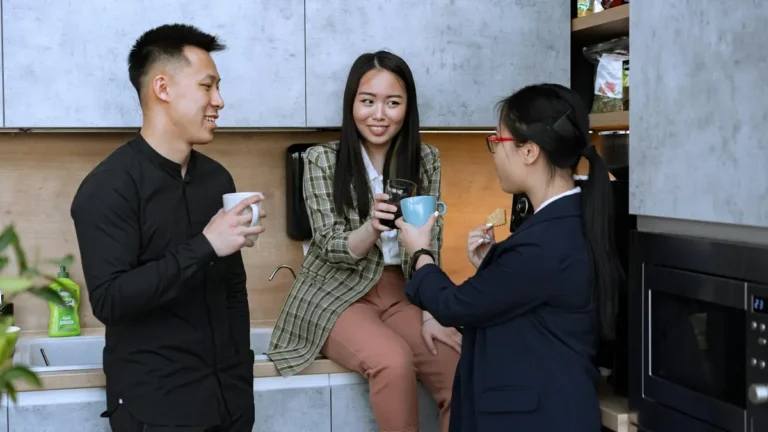 Office colleagues enjoy a coffee break in the kitchen, engaging in friendly conversation.