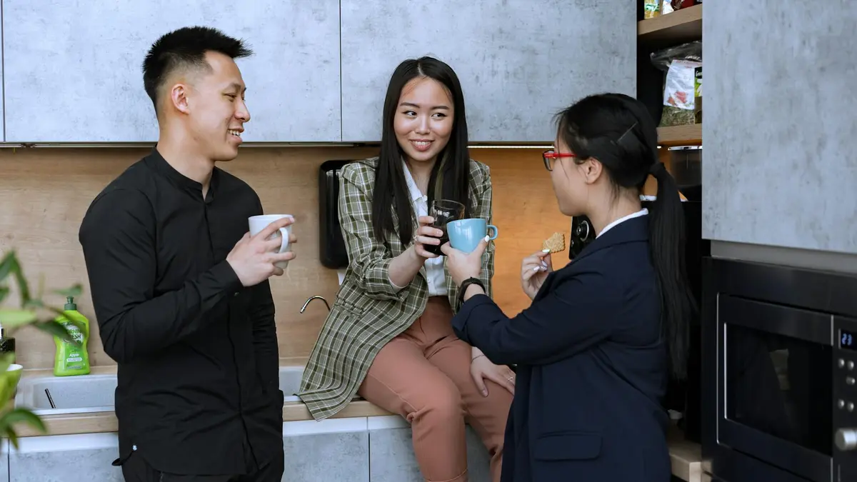 Office colleagues enjoy a coffee break in the kitchen, engaging in friendly conversation.